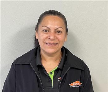 Female employee in black shirt standing in front of a green background.